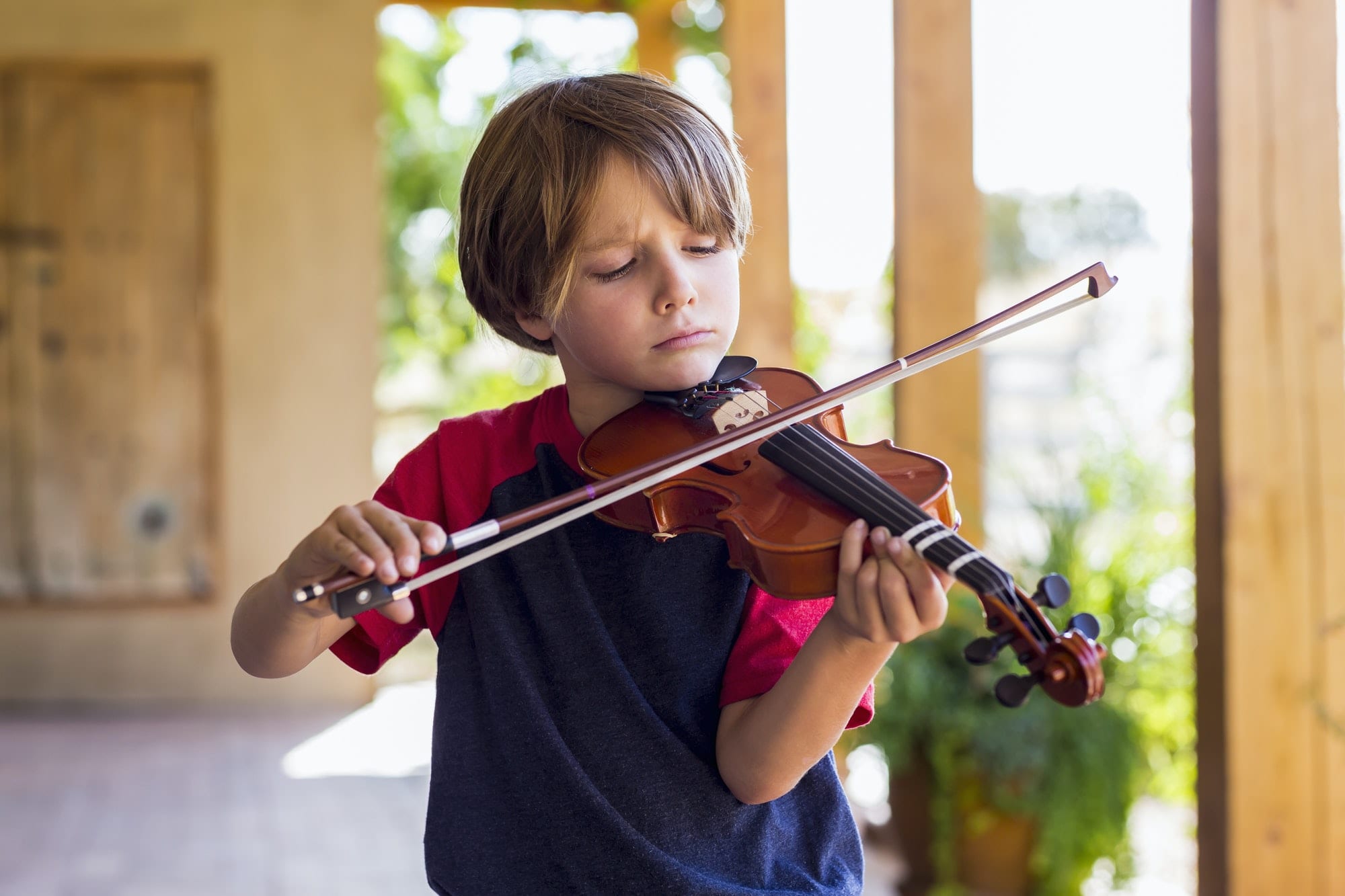 6 year old boy playing violin outside in garden
