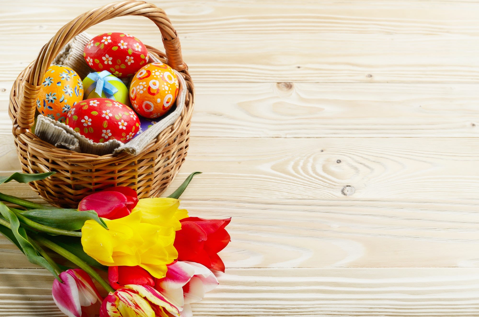 Easter eggs in wicker basket and colorful tulip flowers on woode